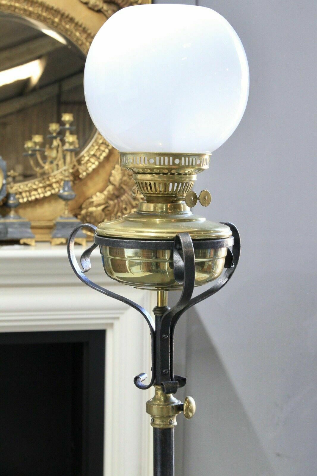 Close-up of brass font, scrolled iron cradle and white globe shade, standard lamp