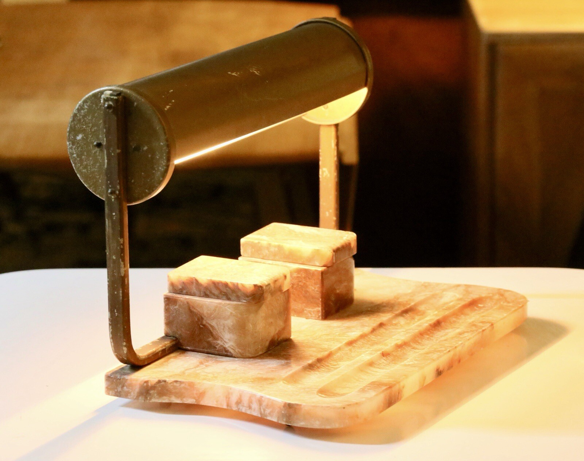 Art Deco alabaster desk lamp switched on, warm glow over the ink stand