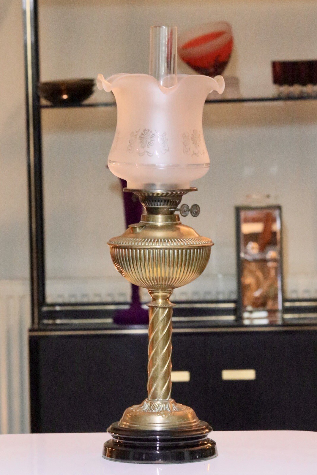 Victorian Art Nouveau brass oil lamp with frosted shade, in front of display shelves