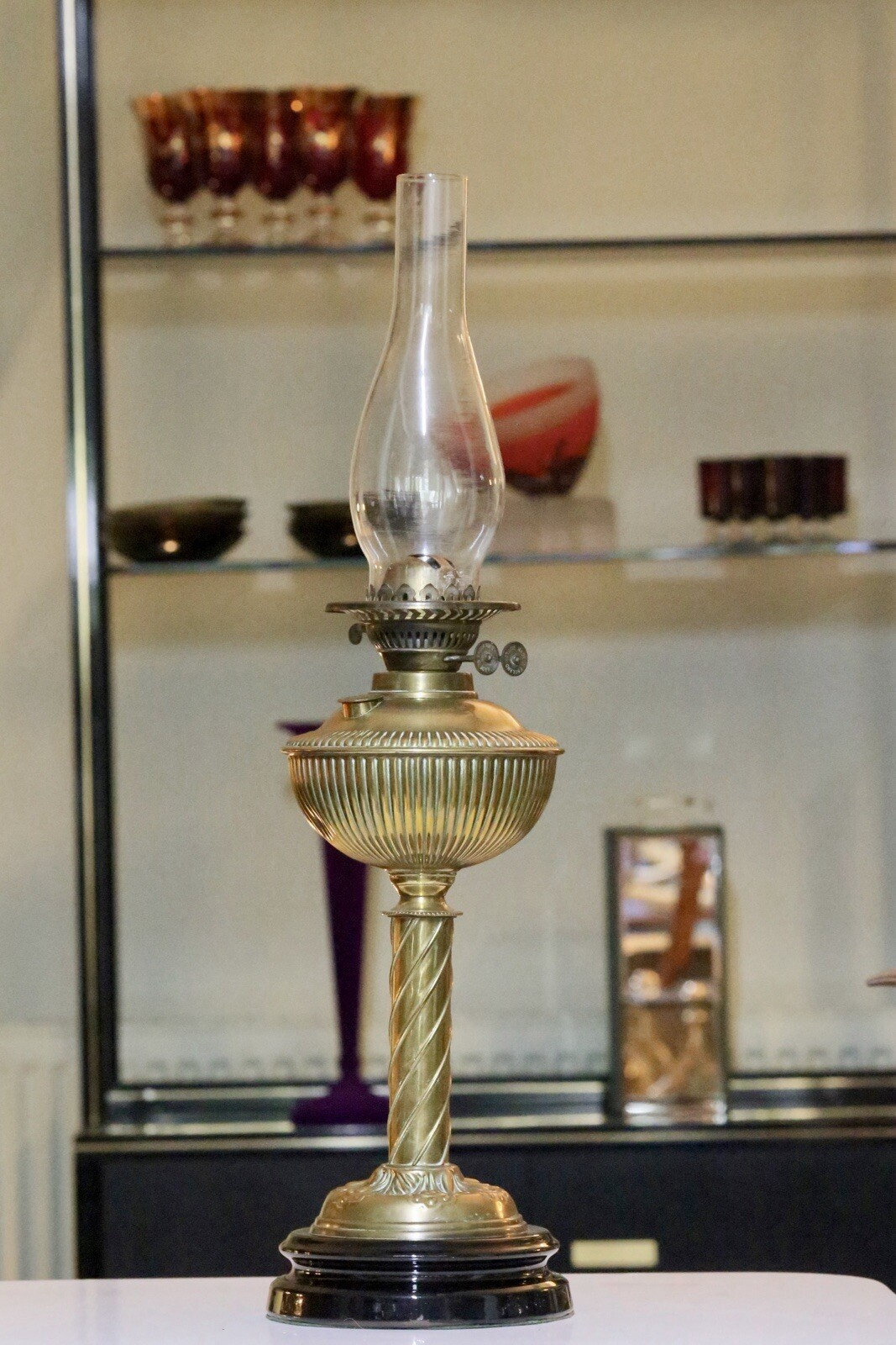 Victorian Art Nouveau brass oil lamp with chimney, in front of display shelves