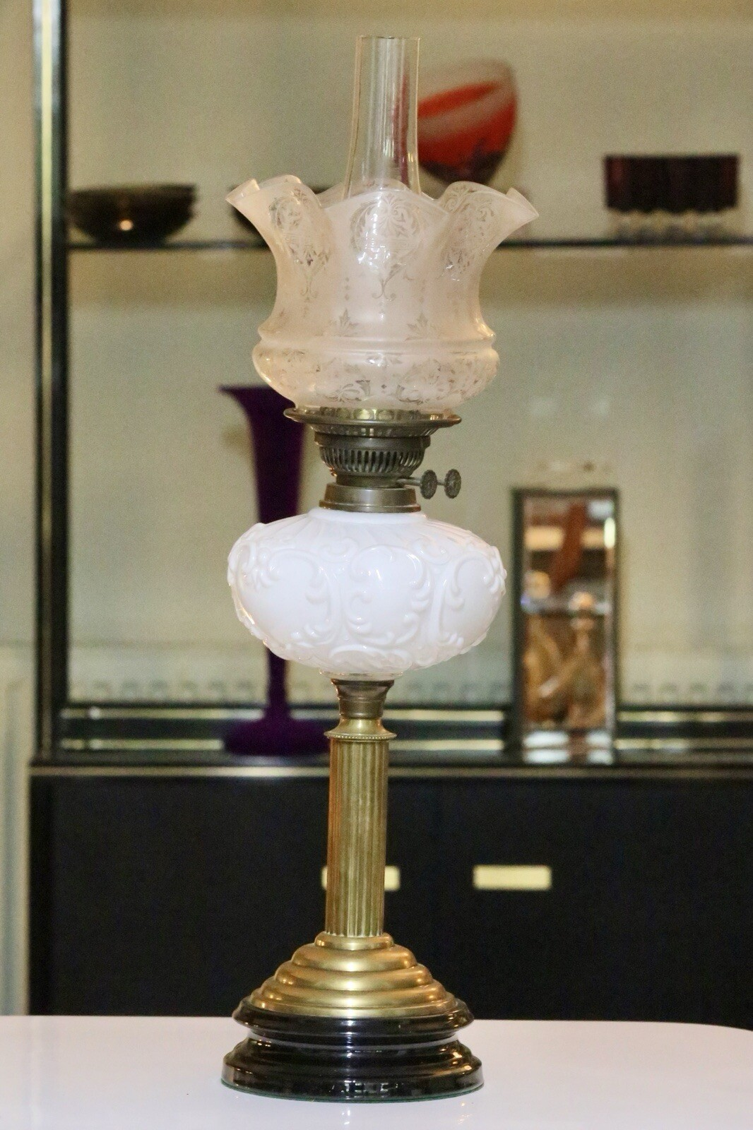 Victorian brass oil lamp with milk glass reservoir in front of display shelves