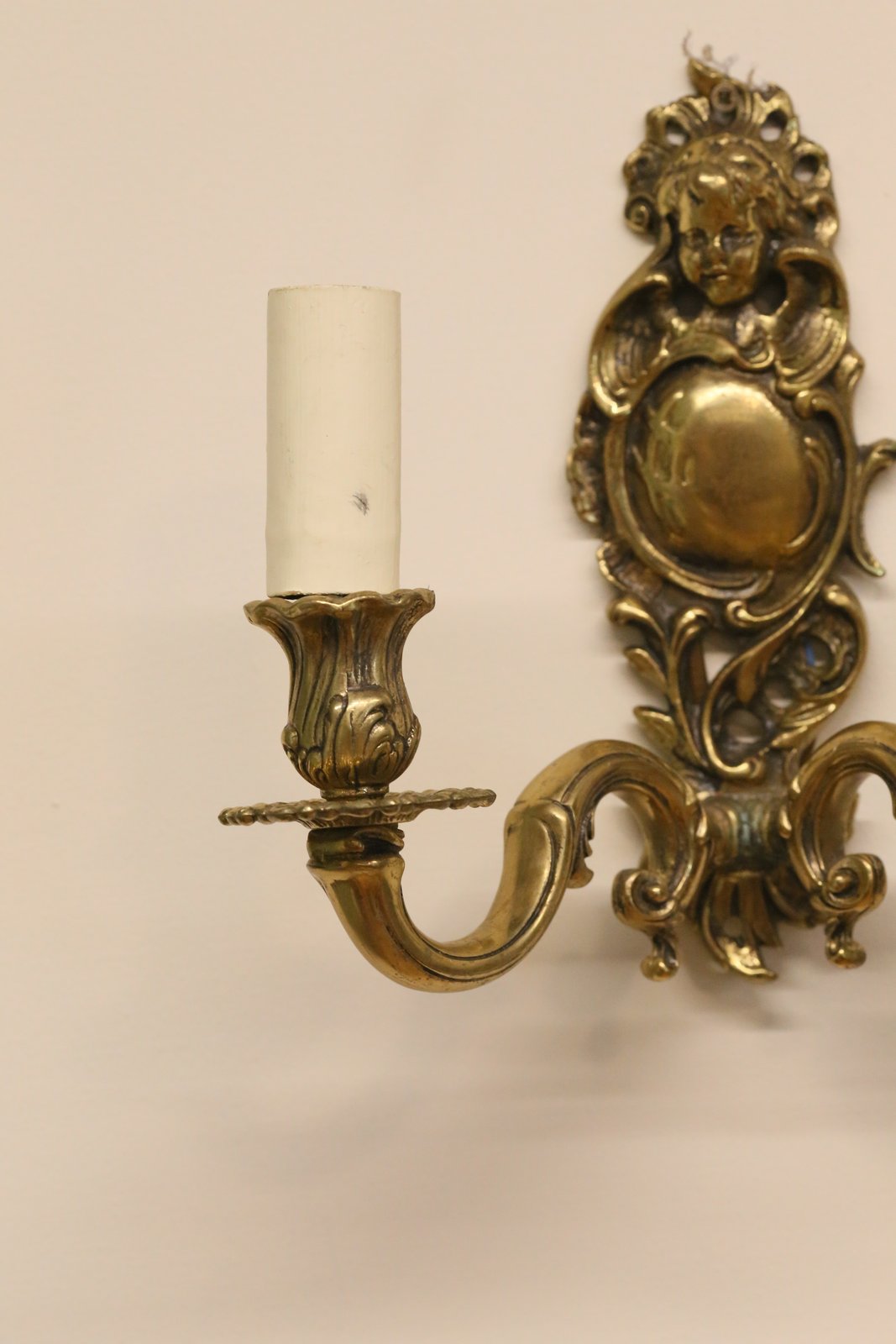 Close-up of brass candle cup and arm, cherub wall sconce
