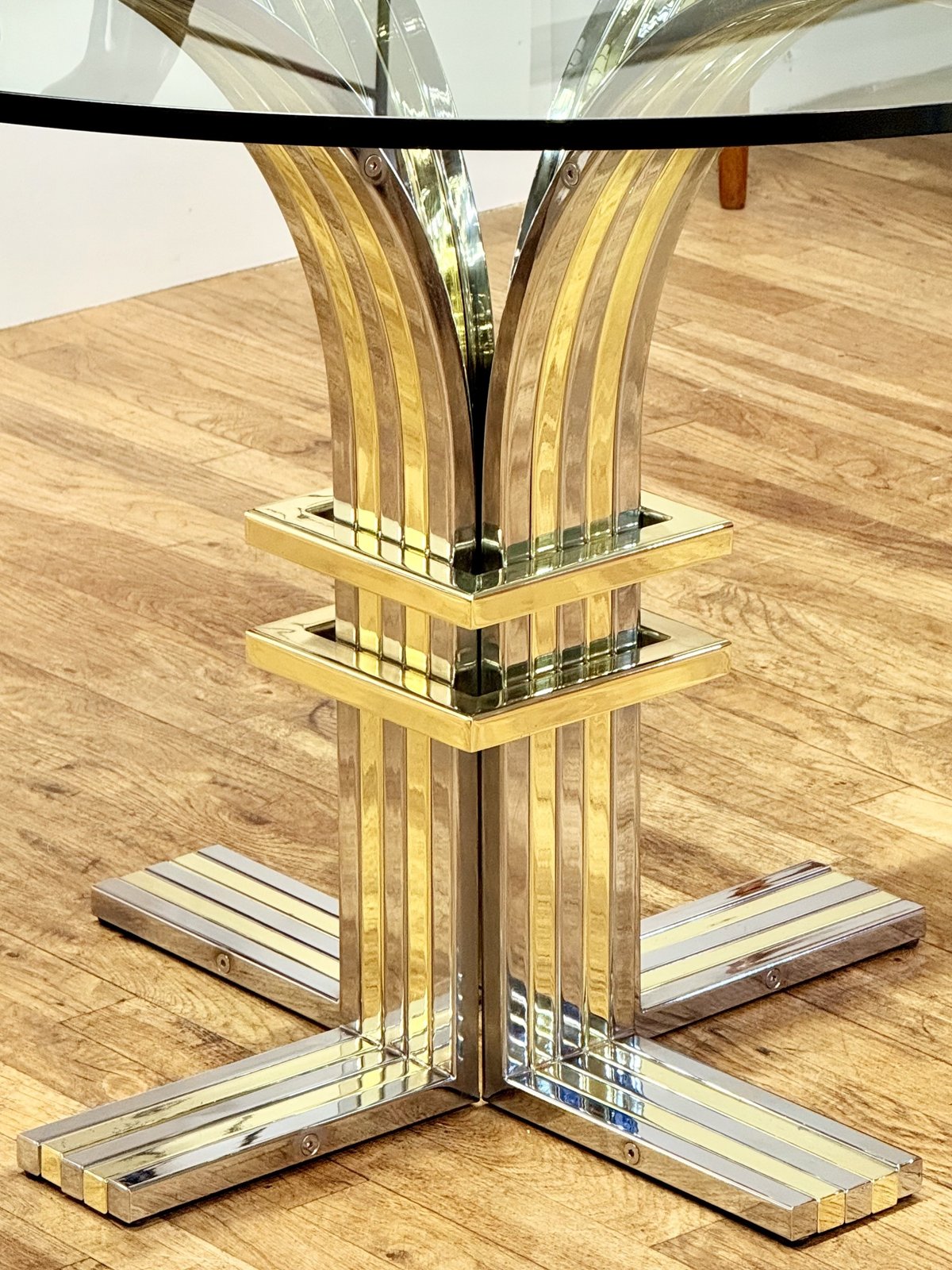 Close-up of flared chrome and brass pedestal under the glass top