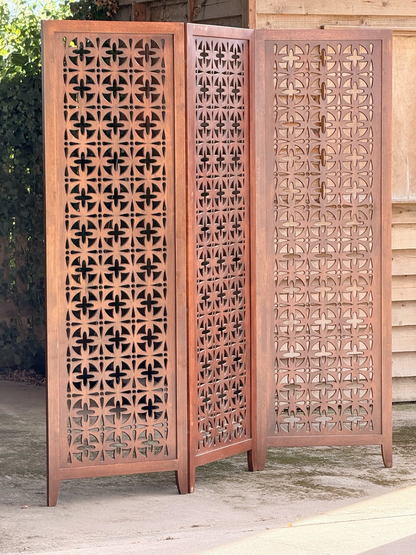Mid-century solid teak three-panel pierced screen, angled view in sunlight