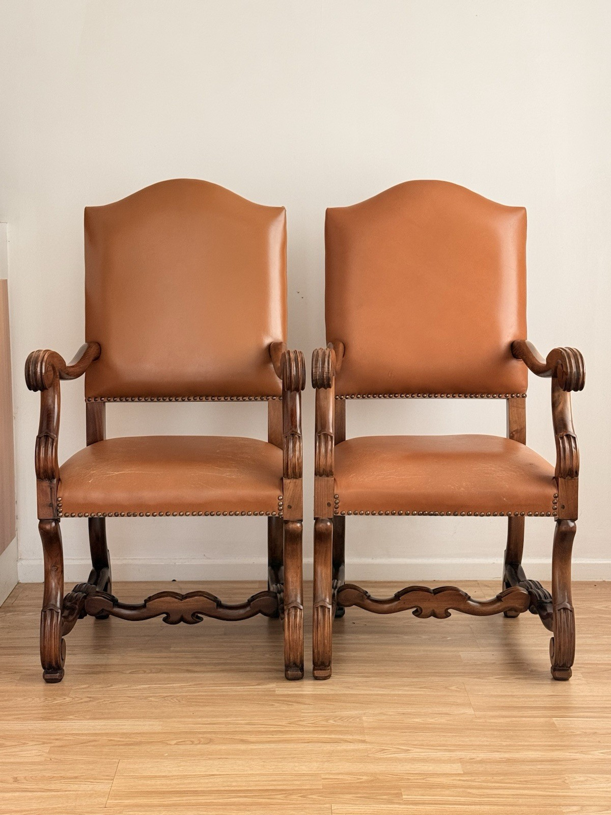 Pair of Spanish Baroque Revival carved wood and leather armchairs, made in Spain, with scrolled arms and tan leather