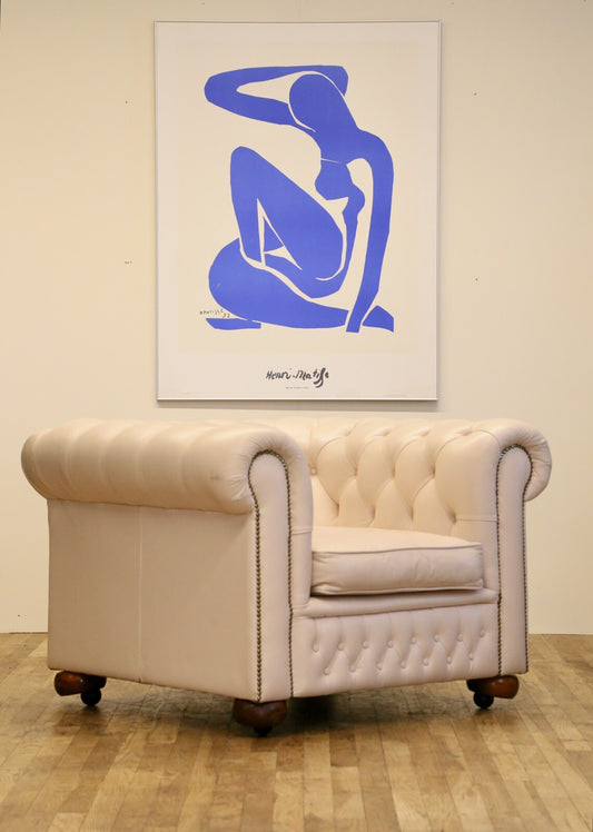 Cream leather Chesterfield club armchair with deep-buttoned back, rolled arms, brass studs and bun feet