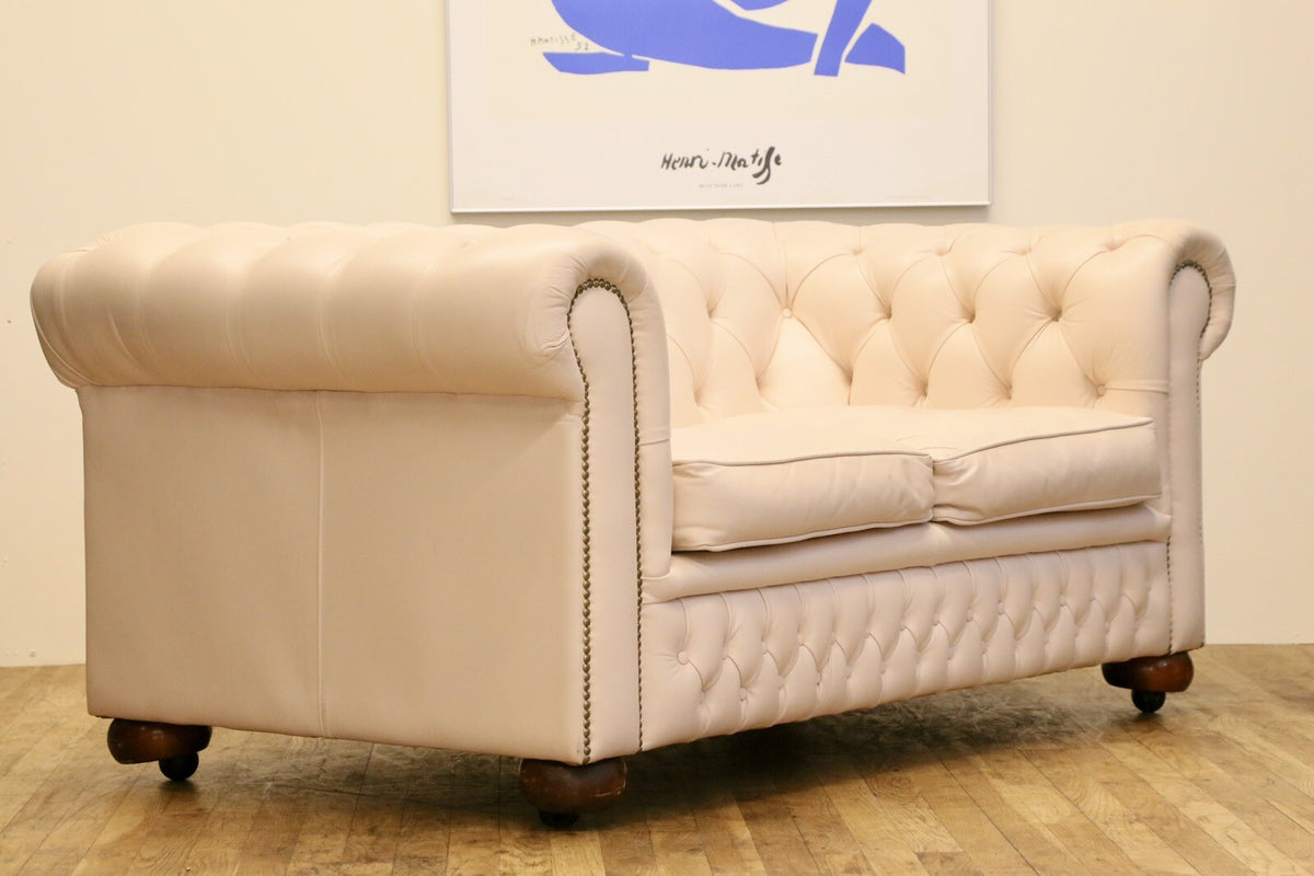 Cream leather Chesterfield 2 seater sofa with deep-buttoned back, rolled arms, brass stud trim and bun feet