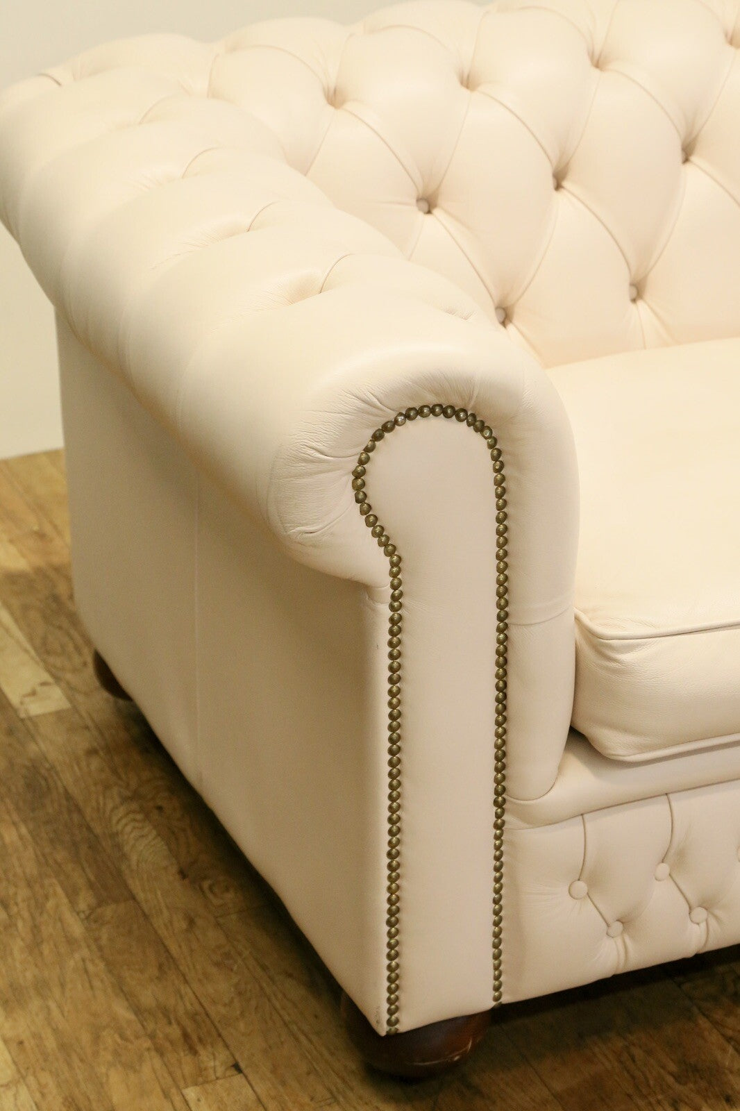 Close-up of rolled arm with brass studs, cream Chesterfield sofa