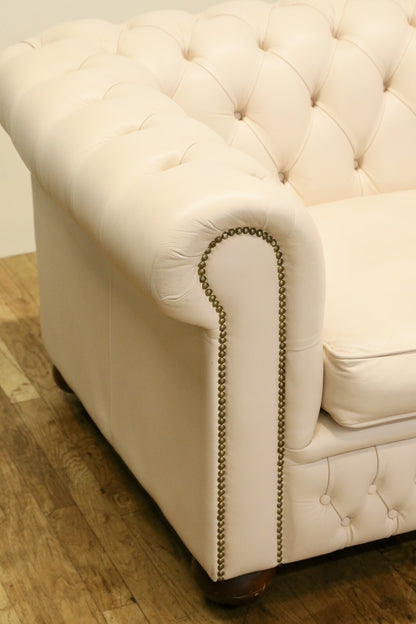 Close-up of rolled arm with brass studs, cream Chesterfield sofa