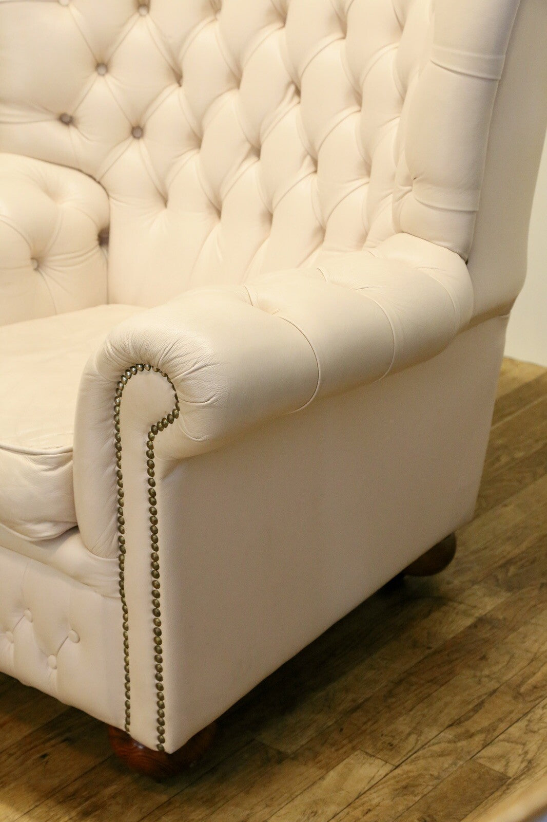 Close-up of rolled arm with brass studs, cream Chesterfield wing chair