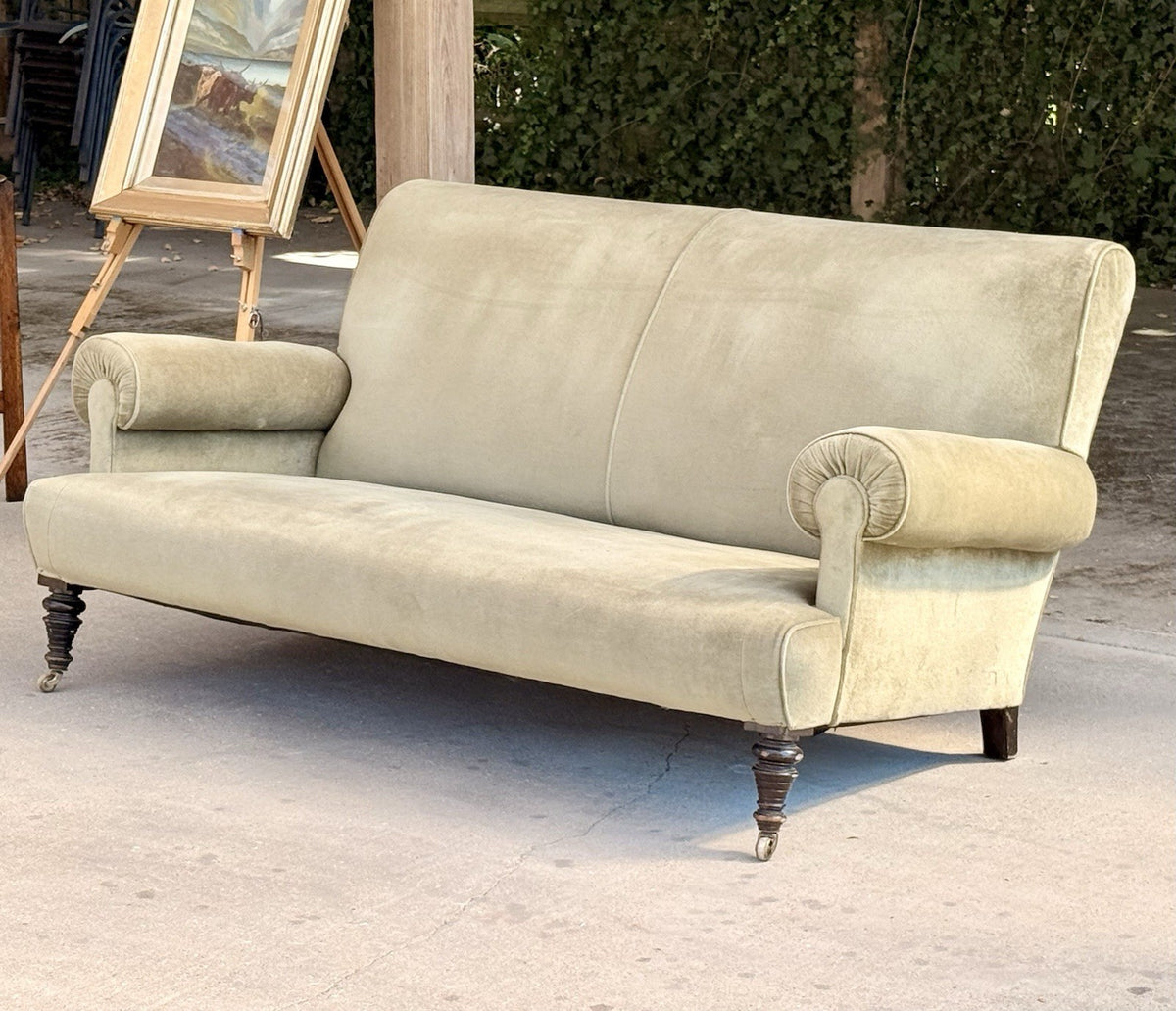 Neo-classical sage velvet sofa, three-quarter view outdoors with an easel behind