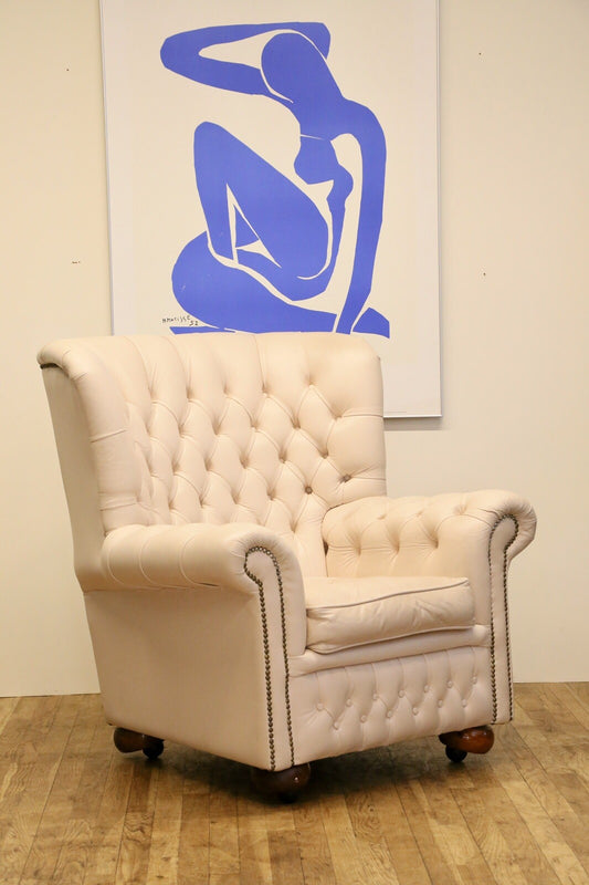 Cream leather Chesterfield wing armchair with deep-buttoned high back, rolled arms, brass studs and bun feet