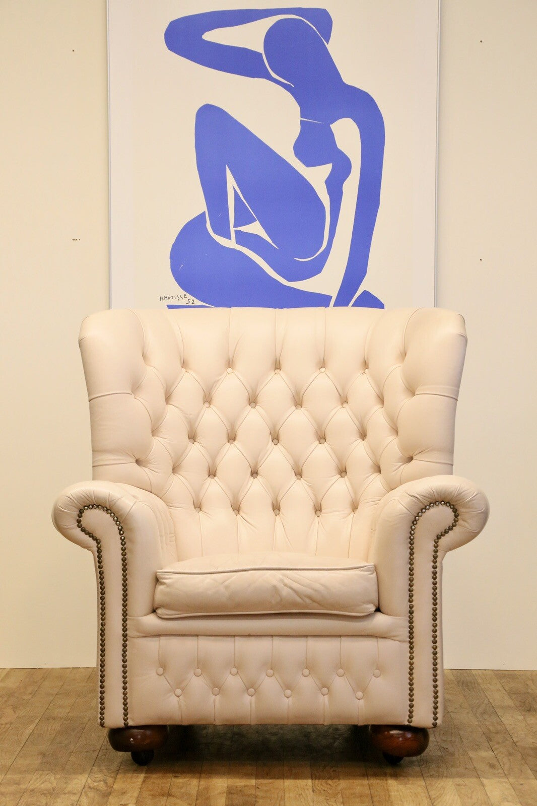 Cream leather Chesterfield wing armchair, front view on wooden floor