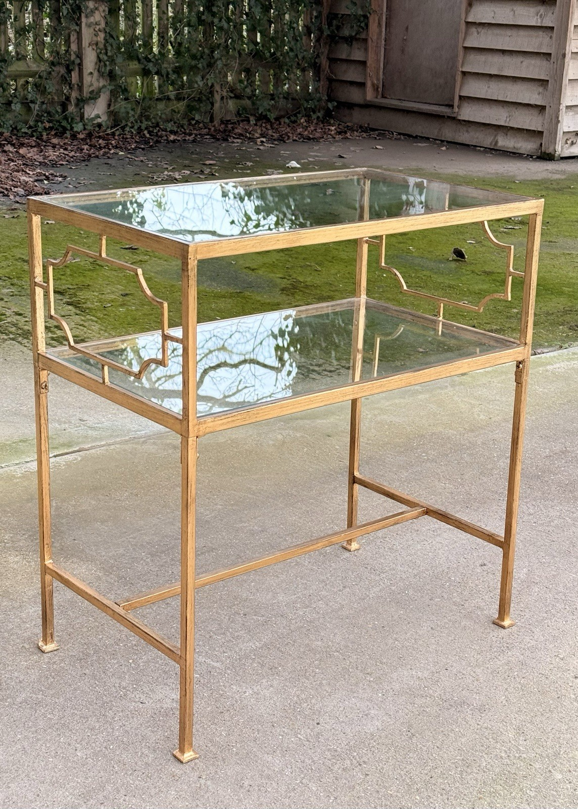 Uttermost Genell gold two-tier glass side table, front view outdoors